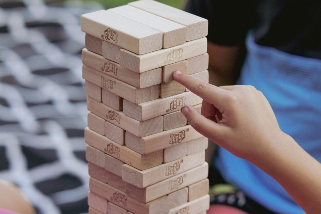 Un enfant joue attentivement au Jenga, en se concentrant sur la précision et l'équilibre, en plein air sur un tapis à motifs.